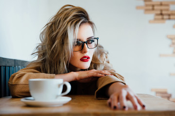 Beautiful fashionable stylish girl sits in a cafe with a cup of coffee.