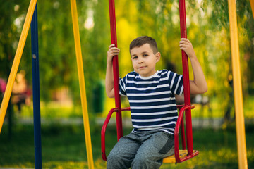 A little boy in a striped T-shirt is playing on the playground, Swing on a swing.