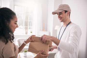 Food delivery. Happy nice person taking the bag while looking at the delivery man
