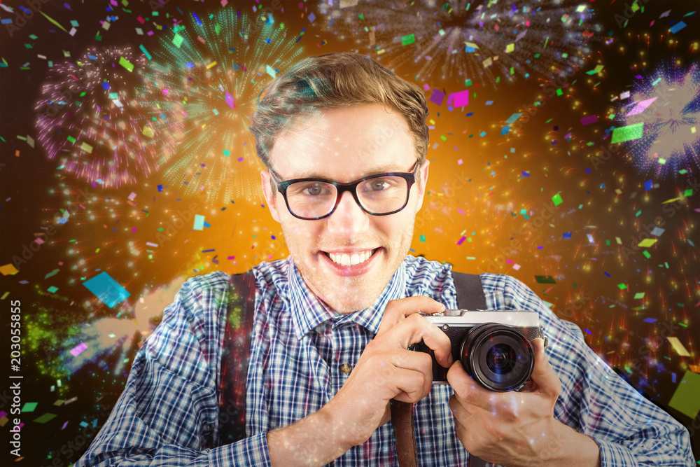 Poster geeky hipster holding a retro camera against colourful fireworks exploding on black background