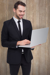 Smiling businessman standing and using laptop against wooden surface with planks