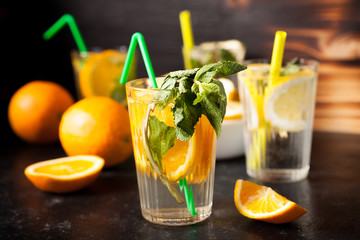 Glasses with natural water with slices of oranges and lemons in it on dark vintage wooden background