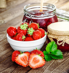 Homemade strawberry jam or marmalade in the glass jar and the basket of ripe strawberries on the wooden table