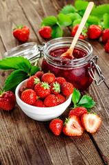 Homemade strawberry jam or marmalade in the glass jar and the basket of ripe strawberries on the wooden table