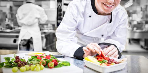 Smiling chef putting a strawberry in the fruit bowl in the kitchen