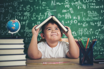 Thoughtful little boy with book in the classroom