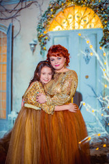 Beautiful red-haired mother hugging daughter, on background of door near house, in winter