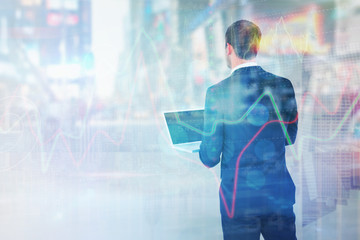 Businessman looking up holding laptop against room with large window looking on city