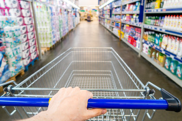 The hand holds the cart in the mall. Holding shopping bags in hand. Man Hand Close Up With Shopping Cart in a Supermarket Walking Trough the Aisle