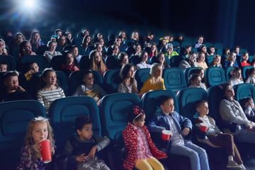 Crowd of people sitting in comfortable seats in modern movie theatre. Children, teens, adults watching  film and sipping fizzy drinks. Concept of cinematography and entertainment. - obrazy, fototapety, plakaty