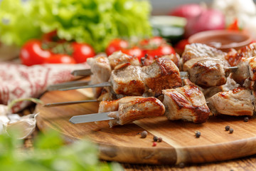 Juicy and mouth-watering shish kebab from pork cooked on open fire and fresh vegetables. Still-life on a wooden background.
