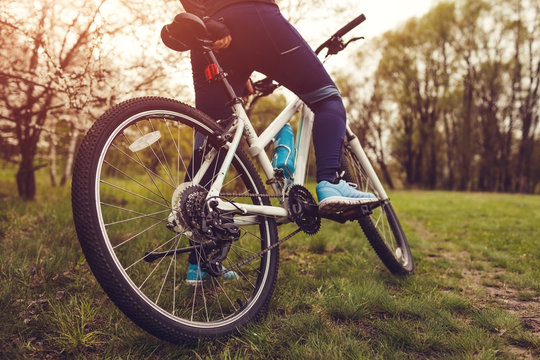 Young woman riding a bicycle in spring forest. Helathy lifestyle concept. Close-up of bike wheel