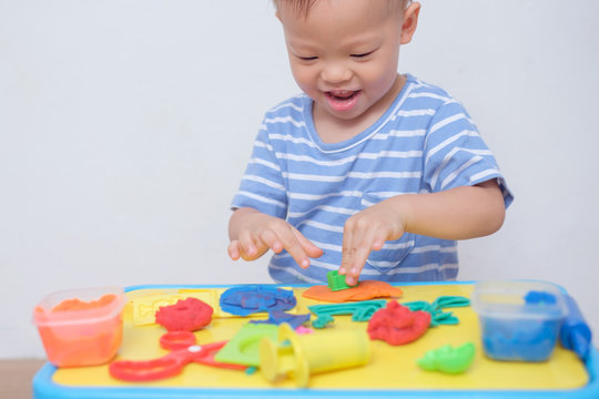Cute smiling little Asian 18 months old toddler baby boy child having fun playing modeling clay / play dought at play school / child care, Montessori education Creative play for toddlers concept