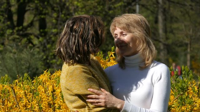 An adult daughter runs up and meets an elderly adult mother hugging her and kissing her. Spring Mother's Day