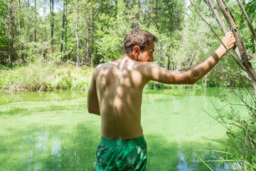 Young man looking at the greenish river a sunny day seen from his back. 