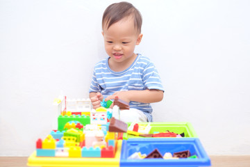 Cute little Asian 18 months / 1 year old toddler boy child sitting on wooden floor having fun playing with colorful building blocks indoor at home, Educational toys for young children concept