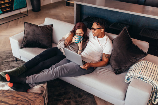 Couple sitting relaxed on sofa and looking at laptop screen