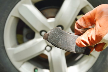 hand in glove holding invalid brake lining for changed on wheel background
