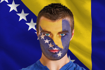 Composite image of serious young football fan in face paint against digitally generated bosnian flag