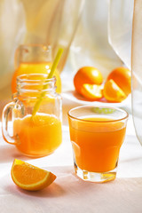 Juicy orange juice in a glass and jug and ripe fruit orange on a white table near the window, the concept of breakfast on a sunny summer day