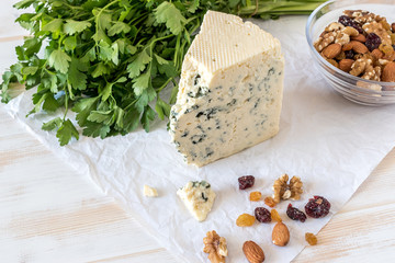 Tasty blue cheese with nuts and herbs on paper on white table