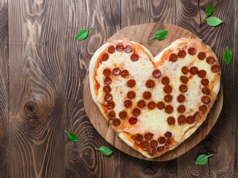 Father's day background with pizza in heart shape and dad word. Pepperoni pizza in heart shape with dad lettering on wooden tabletop. Copy space for text. Father day concept, recipe and idea