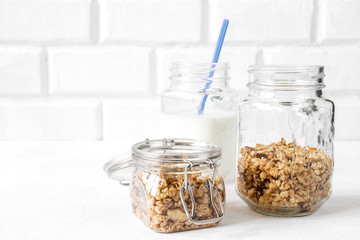 Grnola, raisins, milk in glass jars and various ingredients for a super meal with copy space on a light background