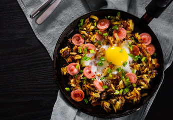 fried egg with sausage and potato in a frying pan on wooden table