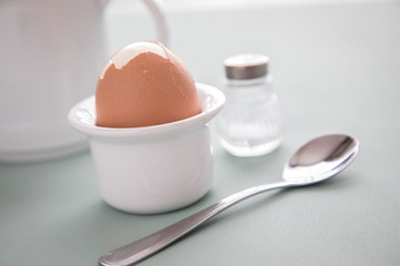 Gekochtes Ei im Becher mit Eierlöffel und Salzstreuer beim Frühstück
