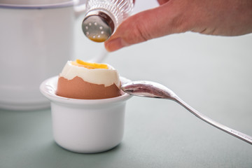 Frau salzt Frühstücksei vom Huhn im Eierbecher mit Salz