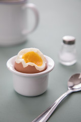 Offenes Ei mit Eigelb im Eierbecher mit Salzstreuer, Eierlöffel und Kaffee