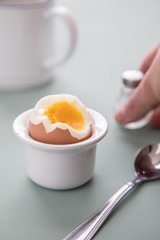 Offenes Ei mit Eigelb im Eierbecher mit Salzstreuer, Eierlöffel und Kaffee