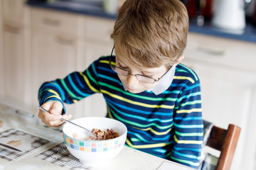 Happy little blond kid boy eating cereals for breakfast or lunch. Healthy eating for children.