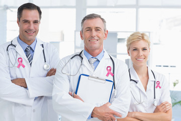 Pink breast cancer awareness ribbon against doctors smiling at camera 