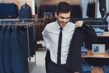 Successful young businessman measures jacket in business mens clothing store.