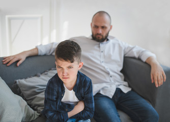 A sad and resentful boy and an angry father in the background.