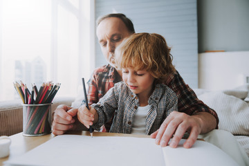 Happy grandfather and small grandson paint with colors.