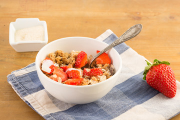 Bowl of cereals with strawberries resting on a blue napkin on a wooden table