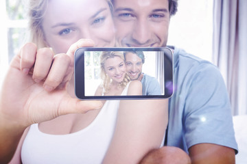 Hand holding smartphone showing against cute young couple relaxing on bed smiling at camera