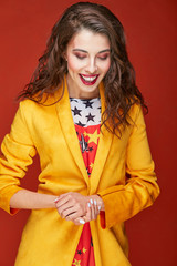 Colorful portrait of beautiful woman with dark brown hair, dressed in bright star print dress and yellow jacket, posing in studio with dark orange background