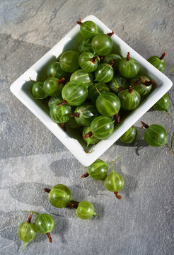 
Gooseberry. Fresh gooseberries in white square plate on gray stone background. Summer berries.  Flat lay. Vertical image.
