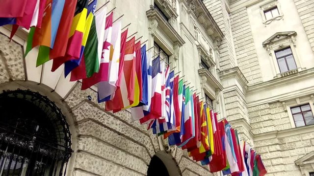 International flags from OSCE and several nations waving in the wind in front of a historical building