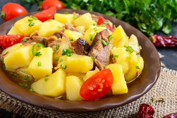 Stewed potatoes with meat in a ceramic bowl on a wooden table.