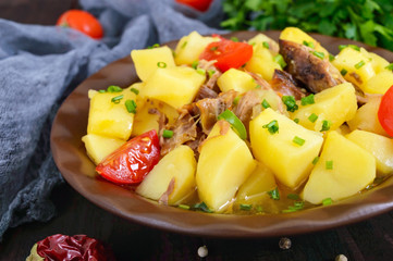 Stewed potatoes with meat in a ceramic bowl on a wooden table.