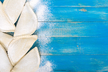 Not fried chebureks in flour on a blue wooden table. Traditional Turkic-Mongolian dish. Frozen semi-finished products. Free space for an inscription.