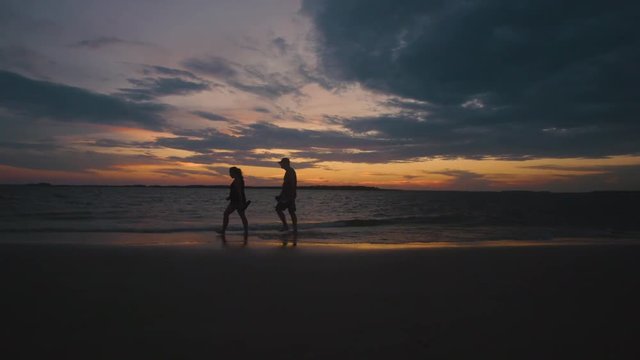 A silhouette of a couple taking a romantic walk down the beach at sunset