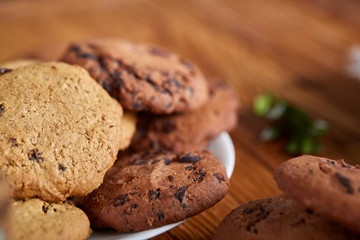 Side view of a plate of chocolate chip cookies on a white plate on wooden background, selective focus