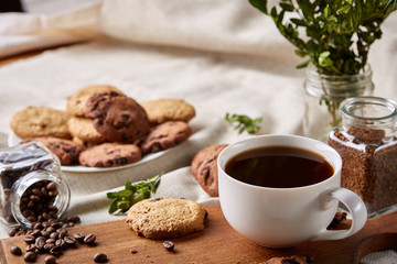 Coffee cup, jar with coffee beans, cookies over homespun tablecloth, selective focus, close-up, top view
