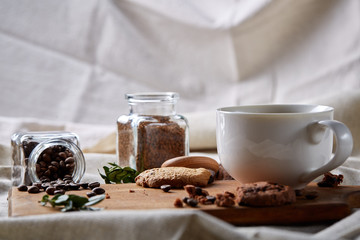 Obraz na płótnie Canvas Coffee cup, jar with coffee beans, cookies over homespun tablecloth, selective focus, close-up, top view