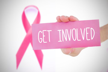 Young woman holding pink  card against pink awareness ribbon